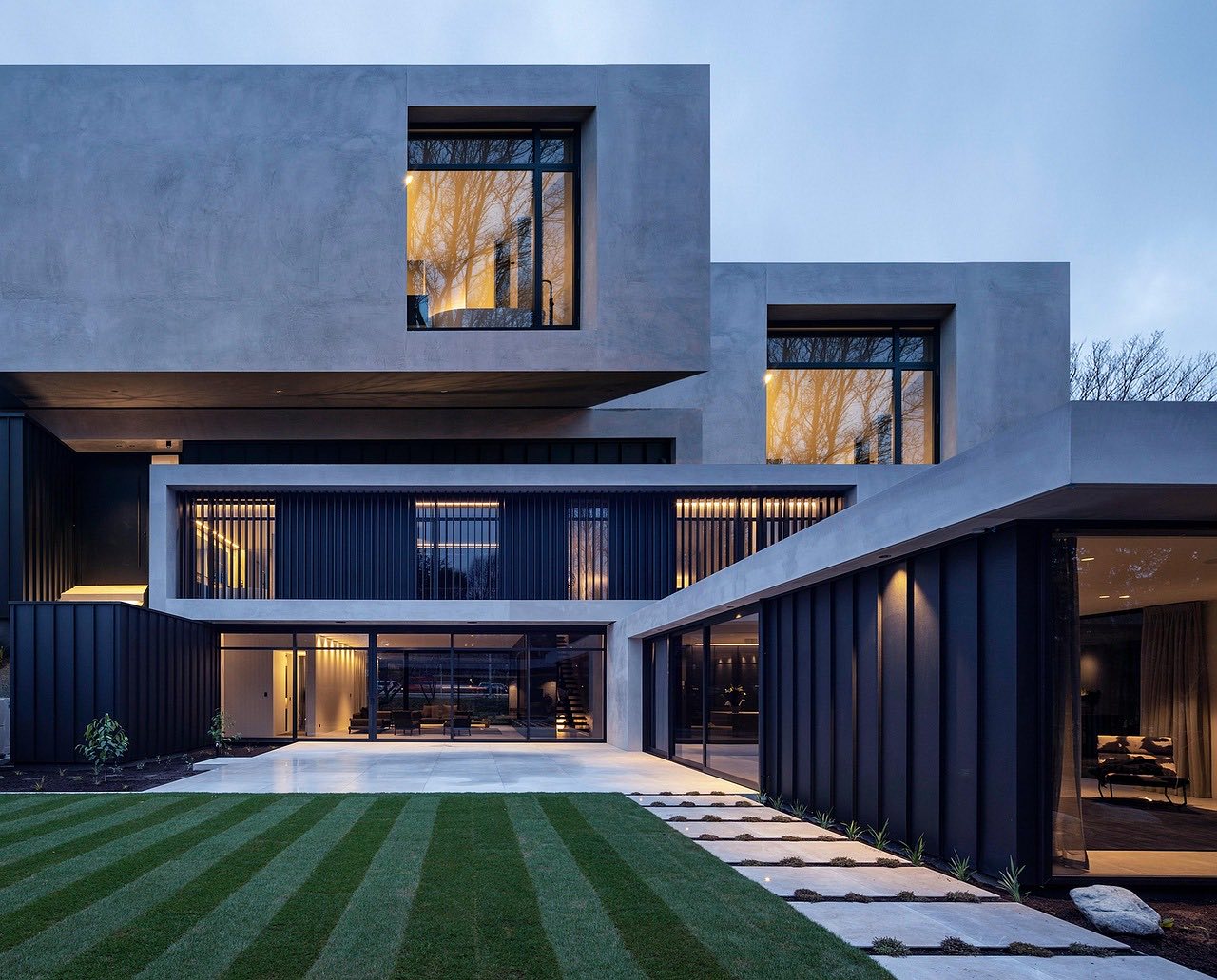 A modern architectural home at dusk with warm-glowing glass, from the Cedar and Stone concept.